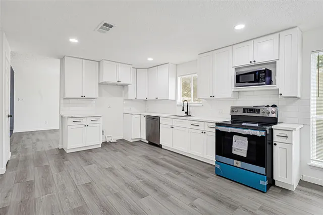 a kitchen with stainless steel appliances white cabinets a sink a stove a refrigerator and white cabinets