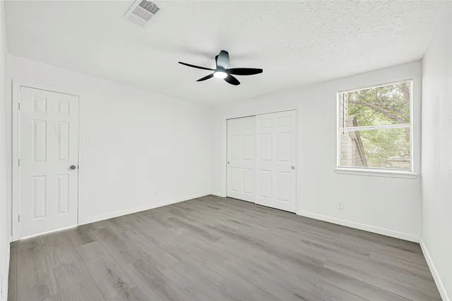 an empty room with wooden floor ceiling fan and windows