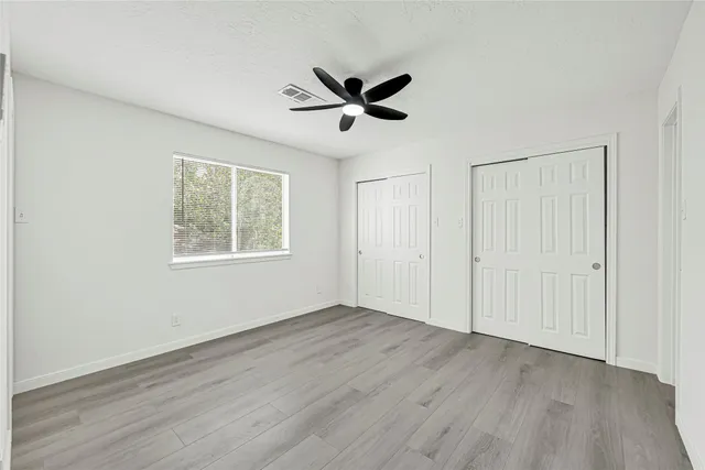 an empty room with wooden floor a ceiling fan and windows