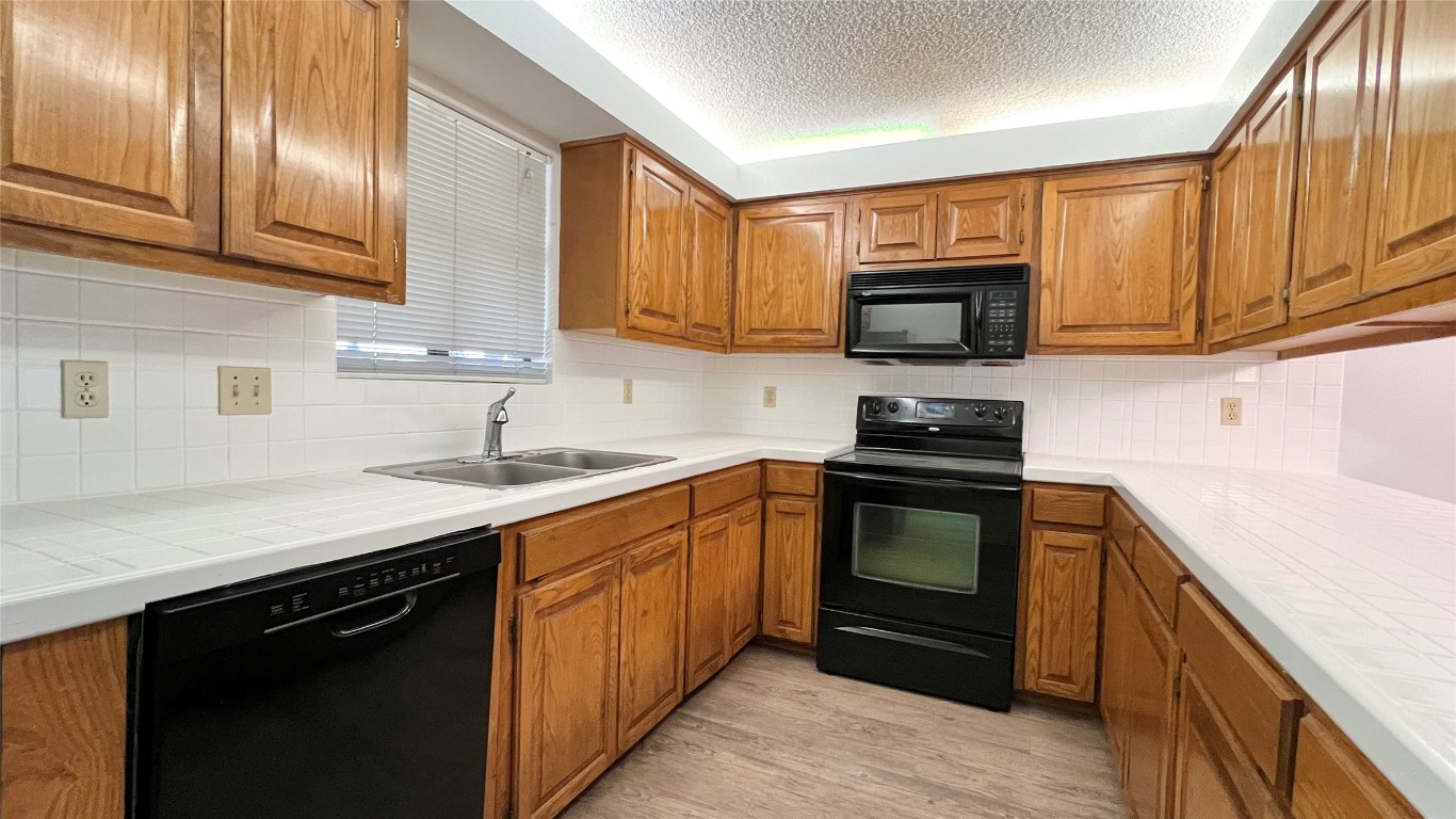 9201 Simmons Road, Unit 101 Austin, TX 78759 - Photo 4 of 10 a kitchen with granite countertop wooden cabinets and a stove top oven