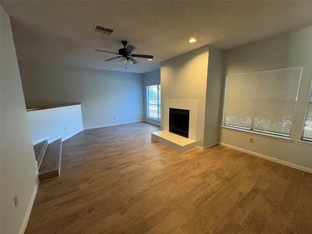 an empty room with wooden floor fan and windows