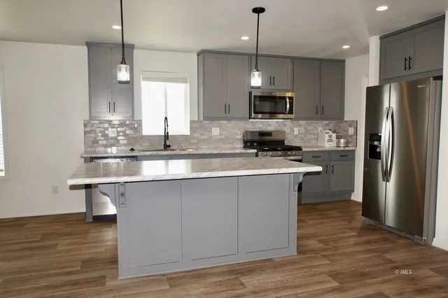 a kitchen with stainless steel appliances granite countertop a sink a stove a refrigerator and island with wooden floor