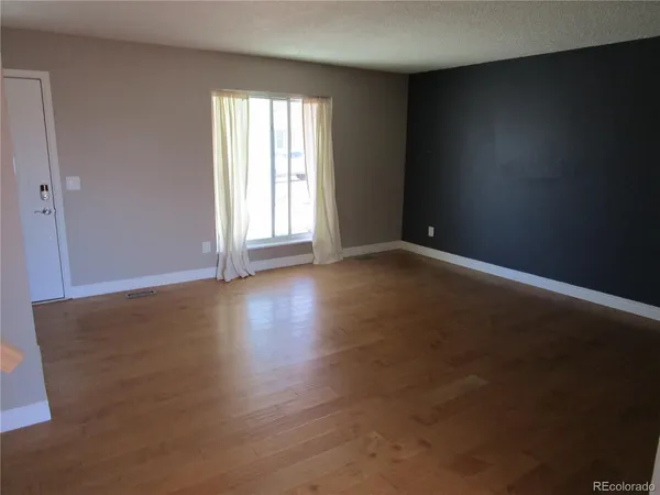 an empty room with wooden floor and windows with curtains