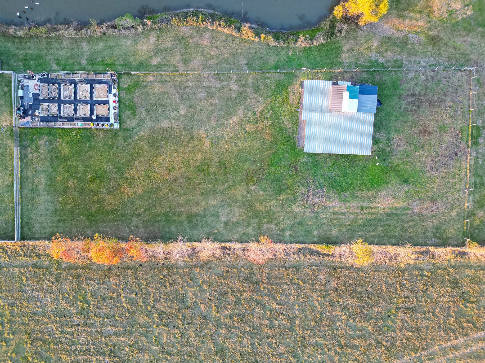 912 County Road 340 Angleton, TX 77515 - Photo 43 of 50 This aerial photo showcases a spacious, fenced property with lush green grass, a sizable outbuilding, and a pond. There's a well-organized garden area, offering ample space for outdoor activities or farming. Ideal for those seeking a blend of rural charm and practicality.
