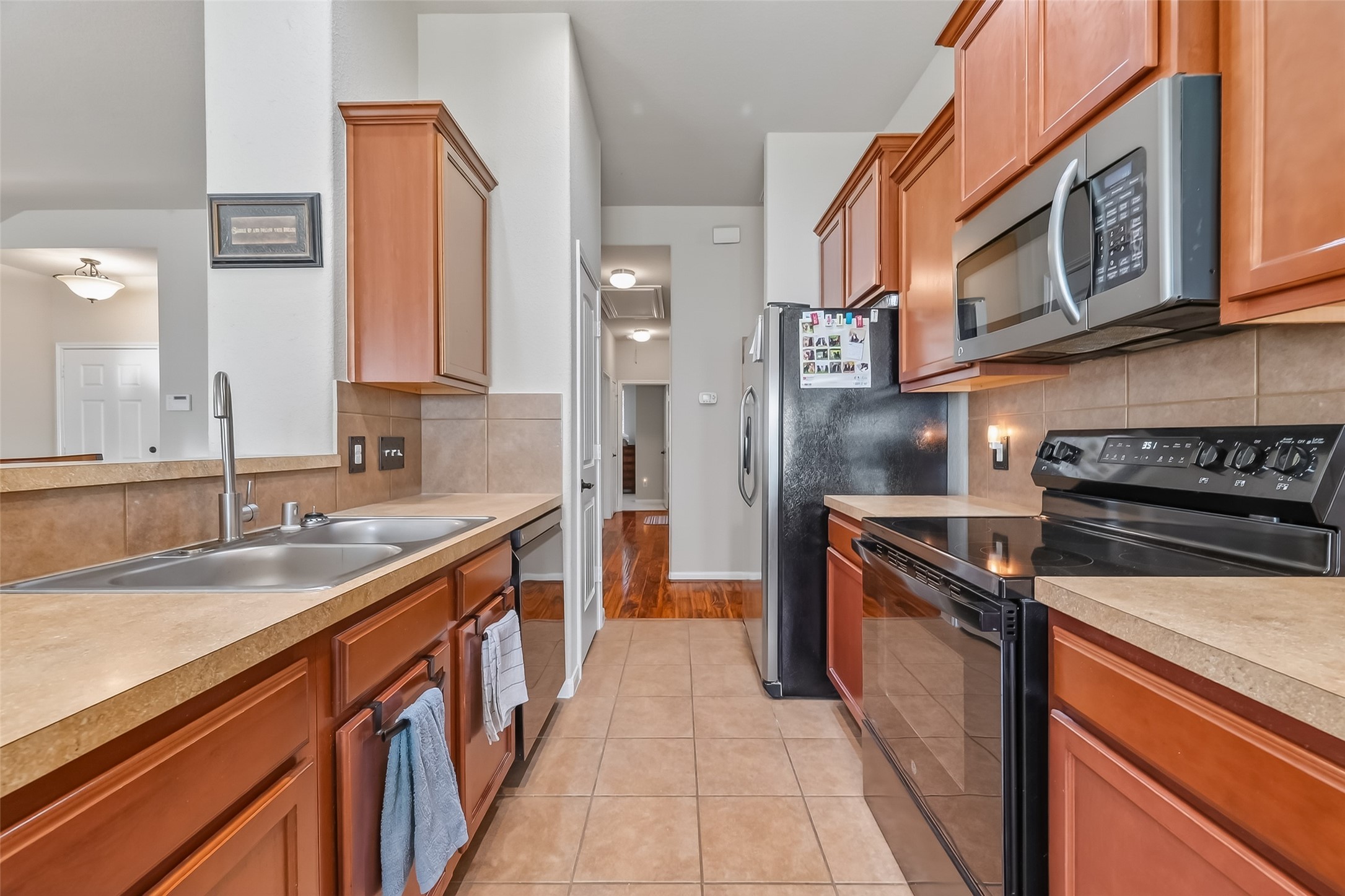 22454 Toronado Ridge Lane Porter, TX 77365 - Photo 12 of 33 This is a modern kitchen featuring stainless steel appliances, wooden cabinetry, and a double sink. The space is well-lit with a combination of natural and overhead lighting, and it opens into a hallway, providing a functional and inviting atmosphere.