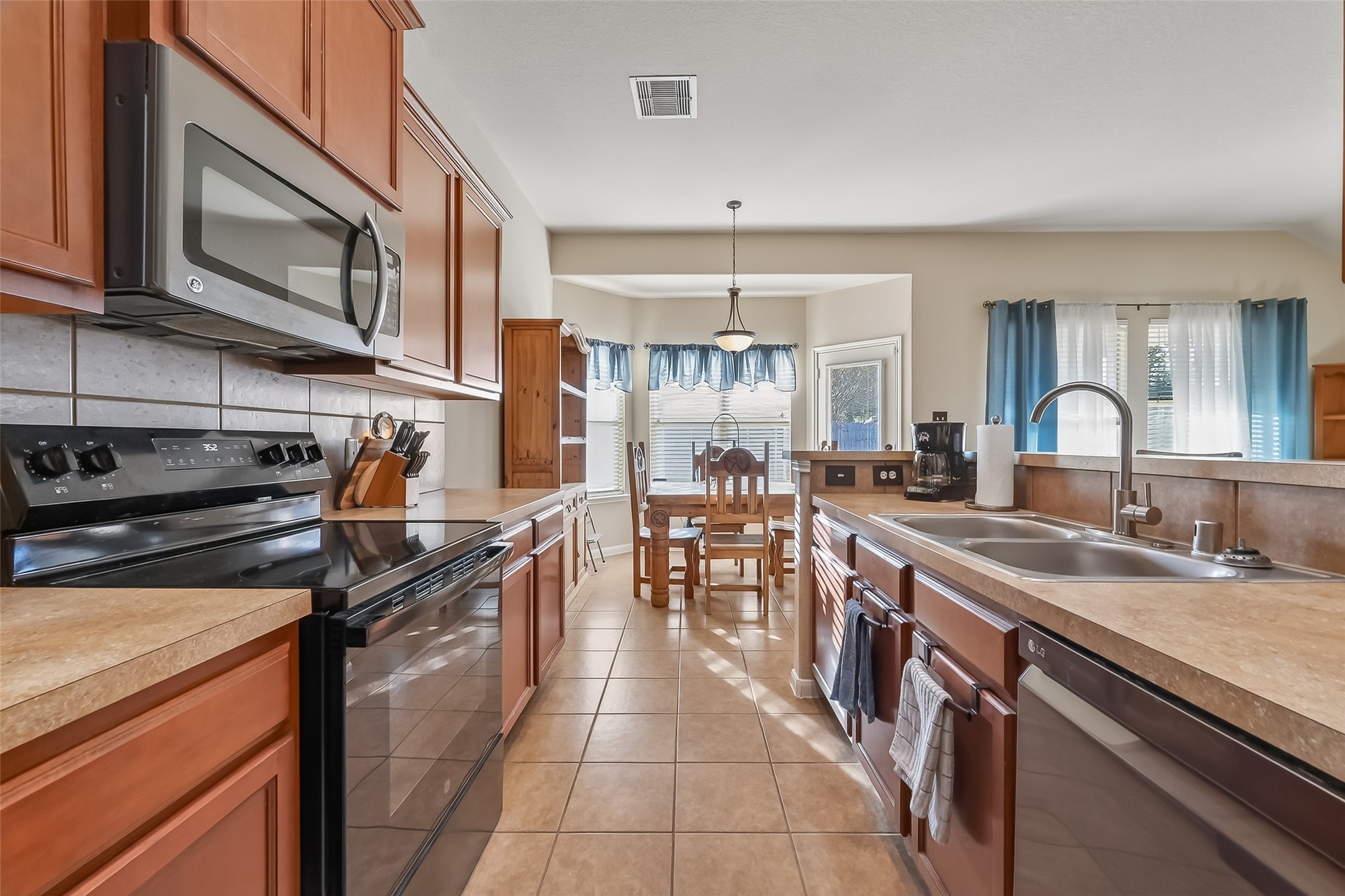 22454 Toronado Ridge Lane Porter, TX 77365 - Photo 15 of 33 This photo showcases a bright, spacious kitchen with warm wood cabinetry, stainless steel appliances, and a double sink. There's a dining area with large windows and ample natural light, creating a welcoming atmosphere.