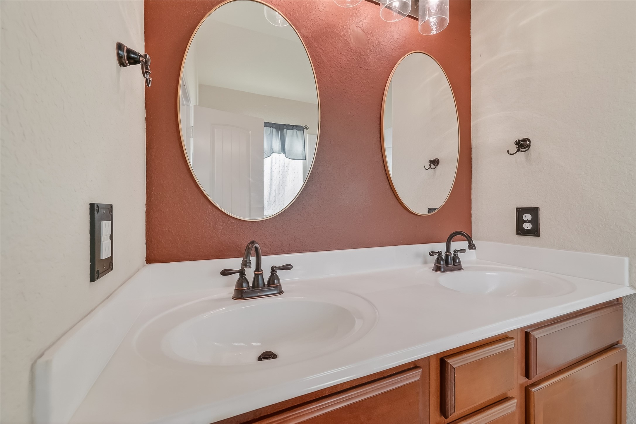 22454 Toronado Ridge Lane Porter, TX 77365 - Photo 24 of 33 This photo shows a bathroom with a double vanity featuring two oval mirrors, modern faucets, and wooden cabinets. The wall has a two-tone design with a warm accent color, enhancing the space's contemporary feel.