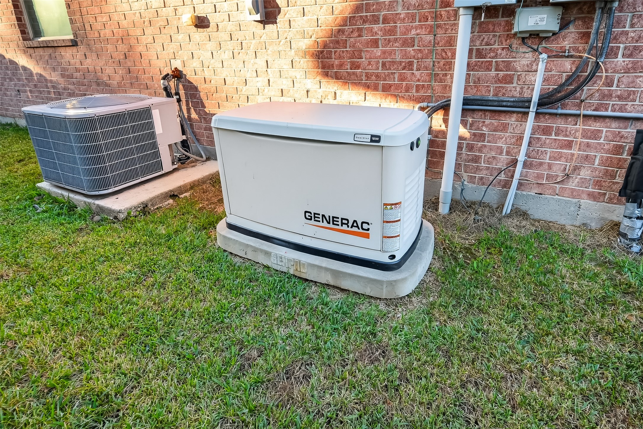 22454 Toronado Ridge Lane Porter, TX 77365 - Photo 33 of 33 This photo shows a Generac standby generator and an outdoor air conditioning unit installed beside a brick house, indicating reliable backup power and climate control features for the home.
