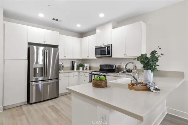a kitchen with a refrigerator a stove a sink and white cabinets with wooden floor