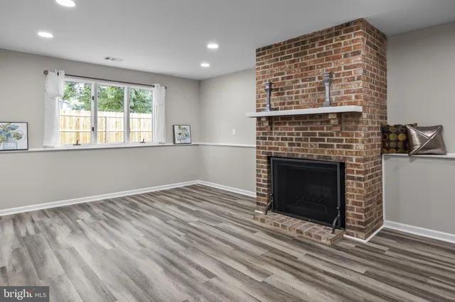 a view of an empty room with wooden floor fireplace and a window
