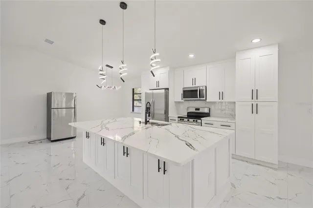 a kitchen with stainless steel appliances kitchen island granite countertop a sink a stove a refrigerator and white cabinets