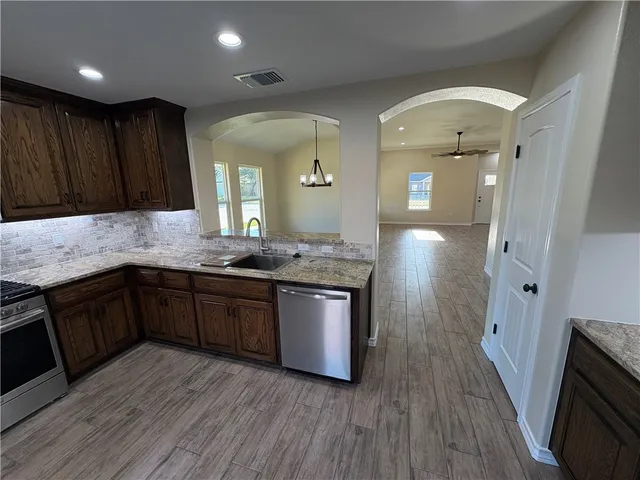 a kitchen with kitchen island granite countertop wooden floors wooden cabinets and stainless steel appliances