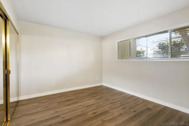 a view of an empty room with wooden floor and a kitchen