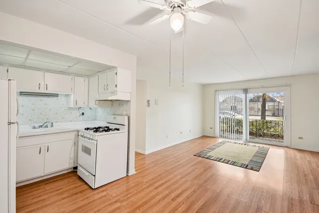 a kitchen with a stove a sink and white cabinets with wooden floor next to windows