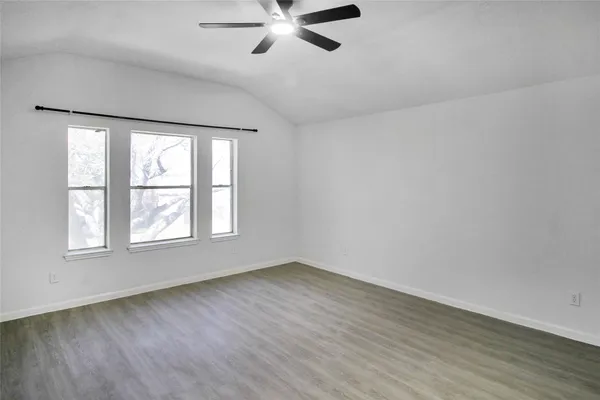 an empty room with wooden floor fan and windows