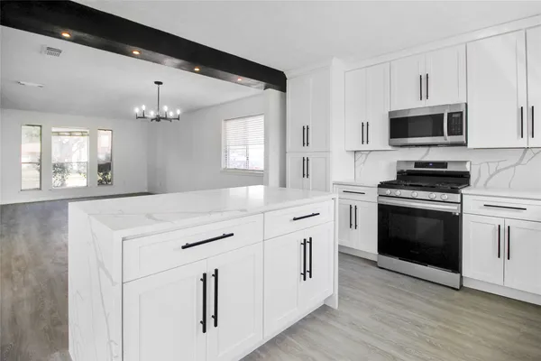 a kitchen with stainless steel appliances white cabinets a sink a stove a microwave and wooden floors
