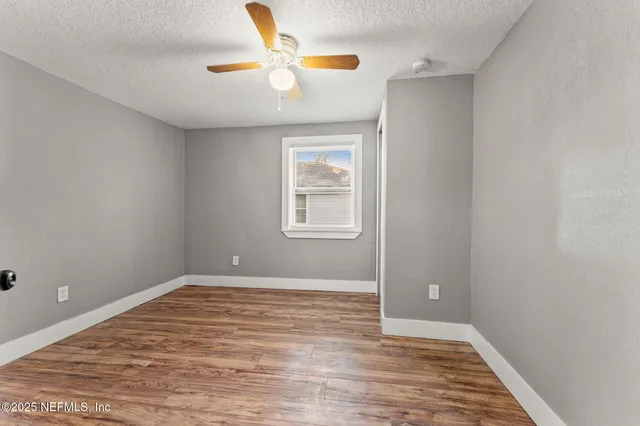 a view of empty room with wooden floor and fan