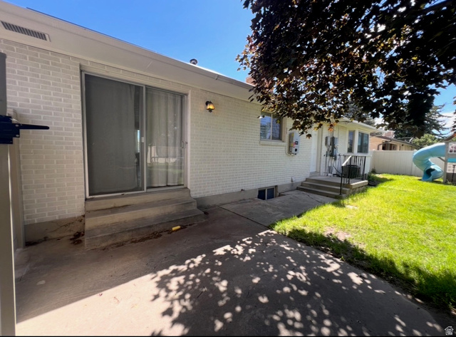 541 Mingo View Avenue Sandy, UT 84070 - Photo 15 of 16 White brick exterior with a sliding glass door, concrete patio, and a manicured lawn