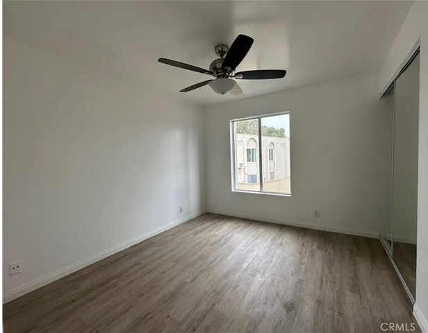 an empty room with wooden floor a ceiling fan and windows
