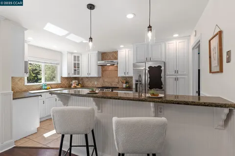 a kitchen with granite countertop a refrigerator a sink and white cabinets