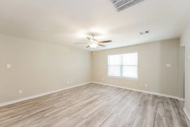 an empty room with wooden floor chandelier fan and windows