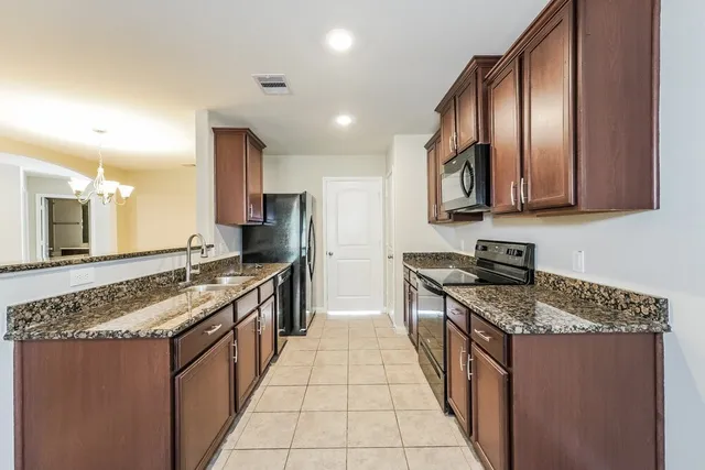 a large kitchen with stainless steel appliances granite countertop a stove a sink dishwasher a refrigerator and a wooden cabinets