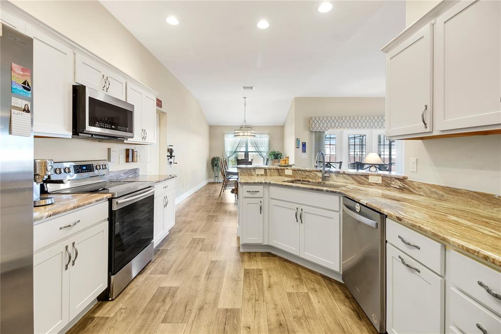 3323 Rohan Road Oxford, FL 34484 - Photo 16 of 46 a large kitchen with stainless steel appliances granite countertop a stove top oven a sink dishwasher and white cabinets with wooden floor