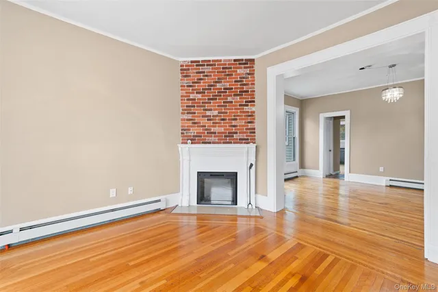 a view of an empty room with wooden floor fireplace and a window