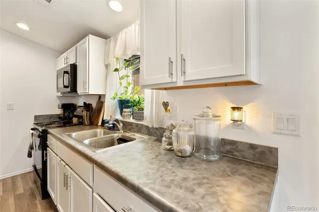 a kitchen with a sink dishwasher and white cabinets with wooden floor