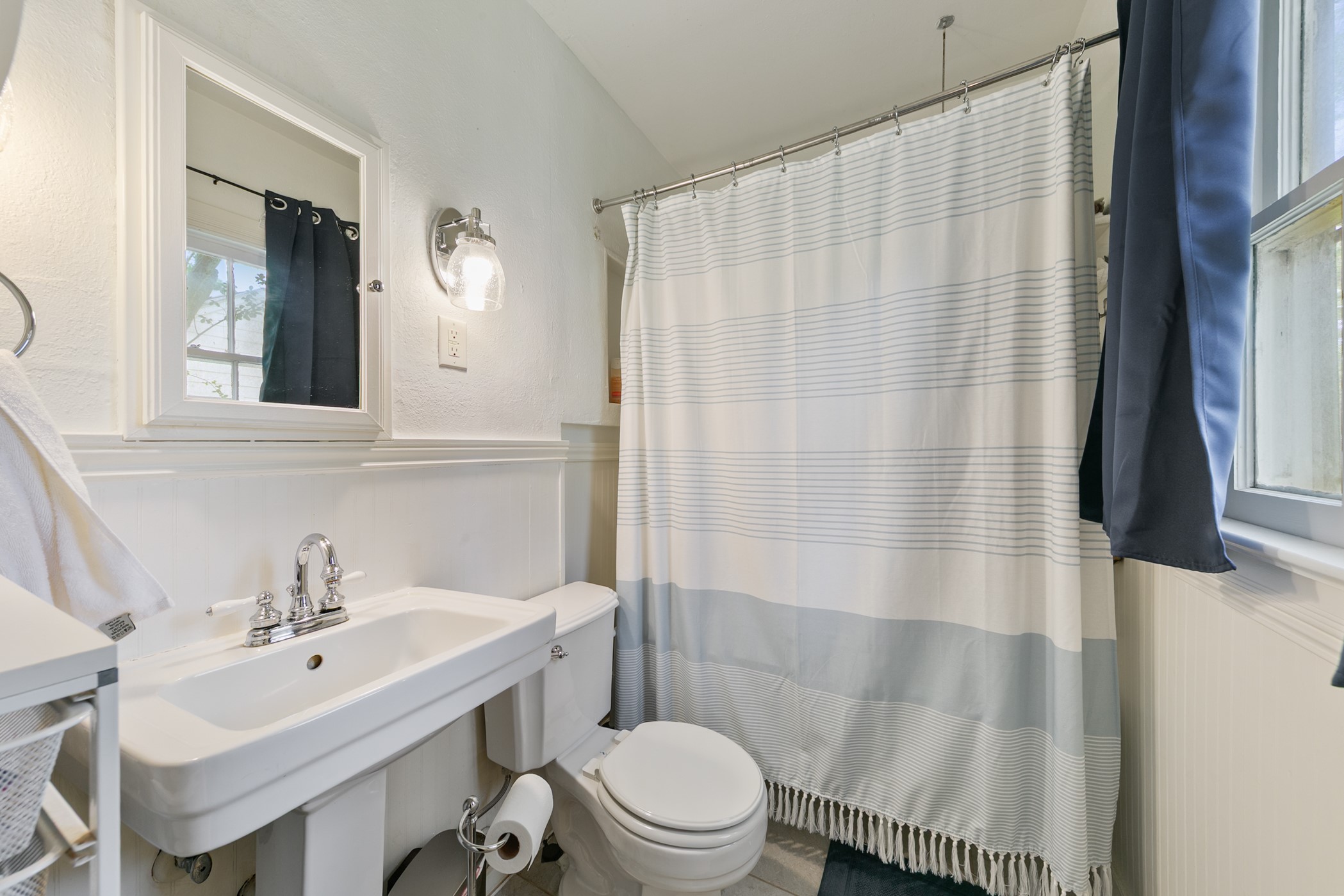 503 West 33rd Street Houston, TX 77018 - Photo 20 of 34 The charm of this 1937 home continues into the ensuite primary bathroom with a pedestal sink, wainscotting, and a clawfoot tub shower combination.