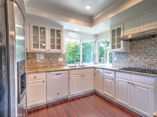 a kitchen with granite countertop white cabinets white appliances wooden floor and a window