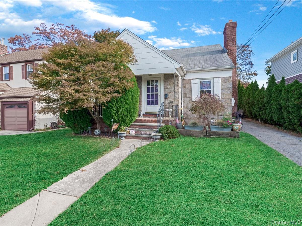Bungalow-style house featuring a chimney, a front yard, stone siding, a shingled roof, and an attached garage