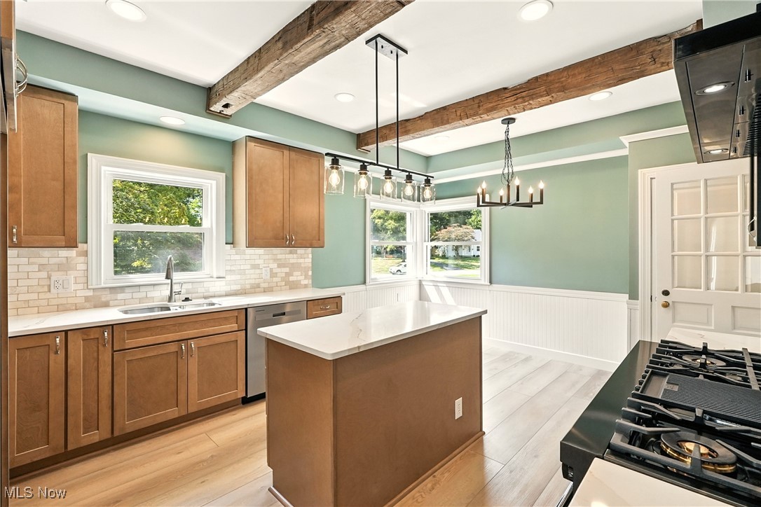 Kitchen featuring brown cabinets, beam ceiling, light wood finished floors, hanging light fixtures, and a center island