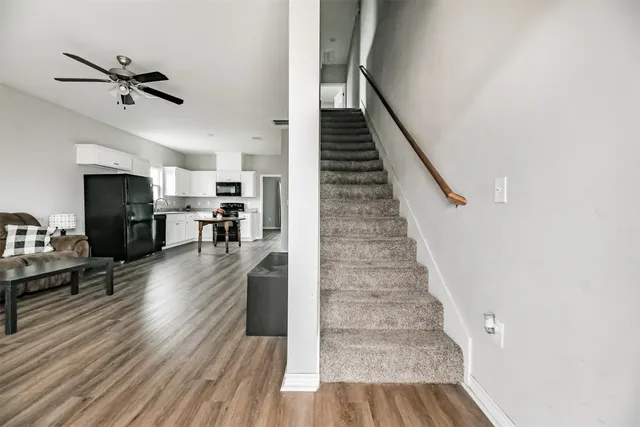 a view of a livingroom with hardwood floor a ceiling fan and staircase