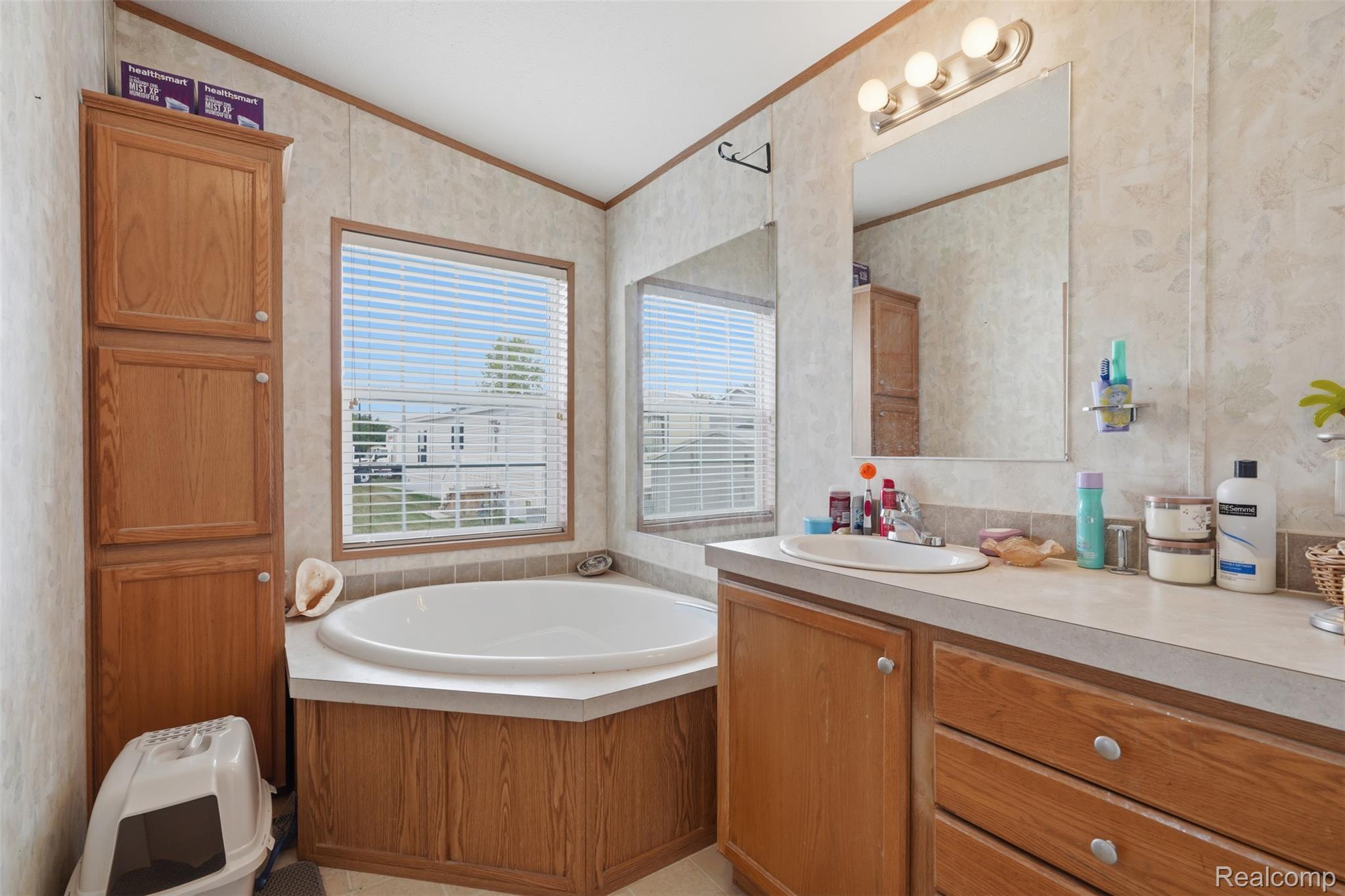 29643 Carousel Street Novi, MI 48377 - Photo 9 of 16 Bathroom featuring a built-in corner soaking tub, a vanity with an integrated sink, a large wall-mounted mirror, and a wood-finish storage cabinet