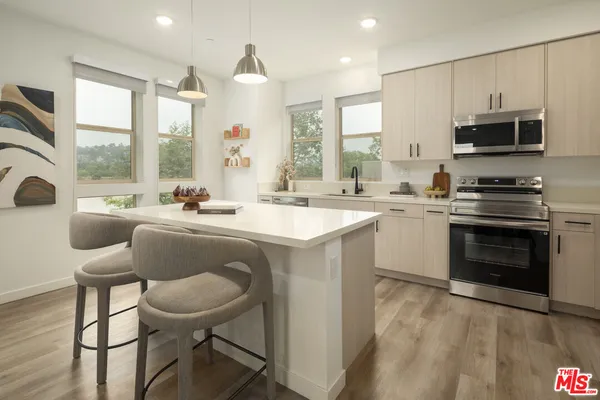 a kitchen with stainless steel appliances a stove a sink dishwasher a microwave oven and a dining table with wooden floor