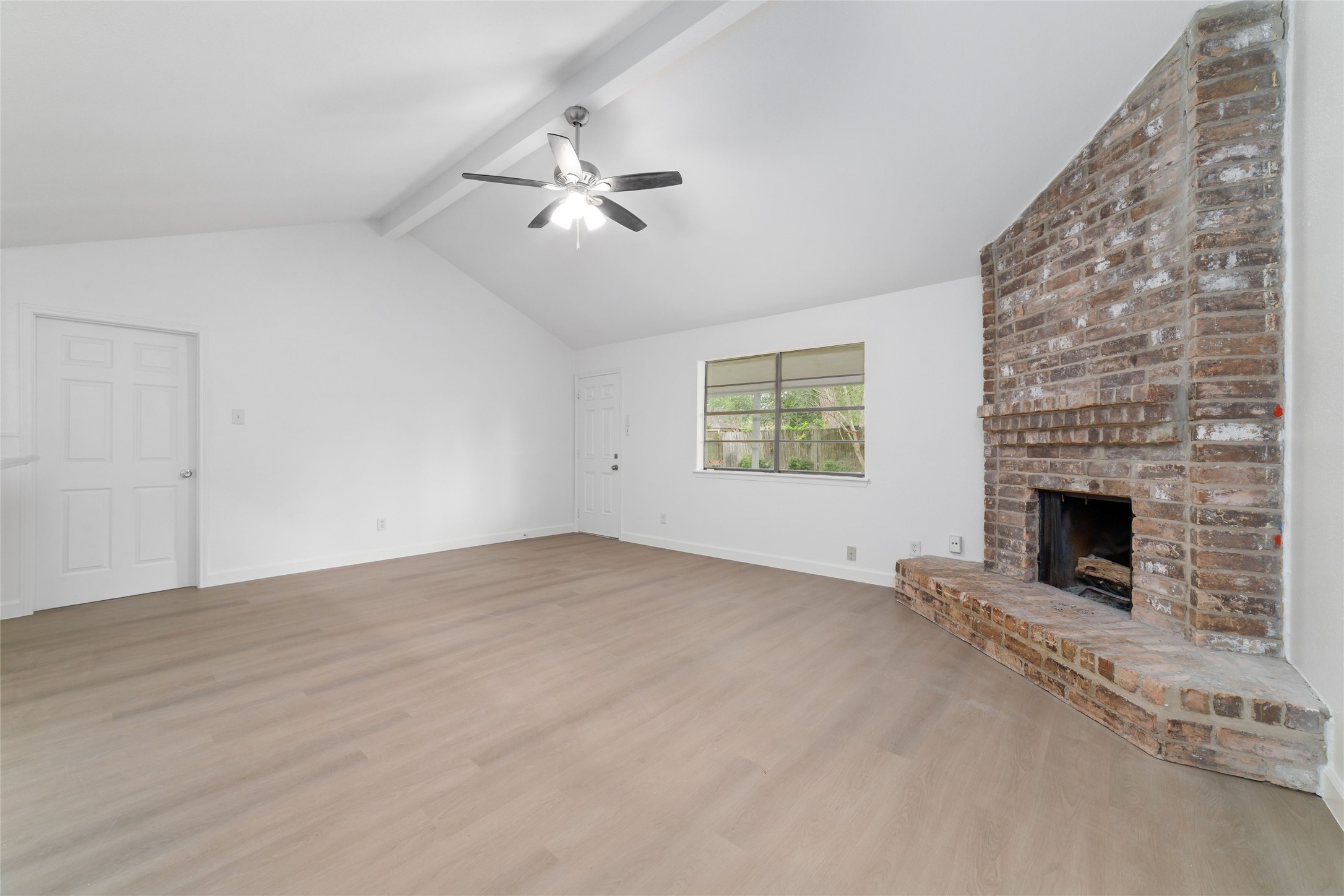 5023 Monteith Drive Spring, TX 77373 - Photo 6 of 20 Inviting living room featuring a cozy brick fireplace, vaulted ceilings, and a ceiling fan, with a large window bringing in natural light and adding warmth to the space.