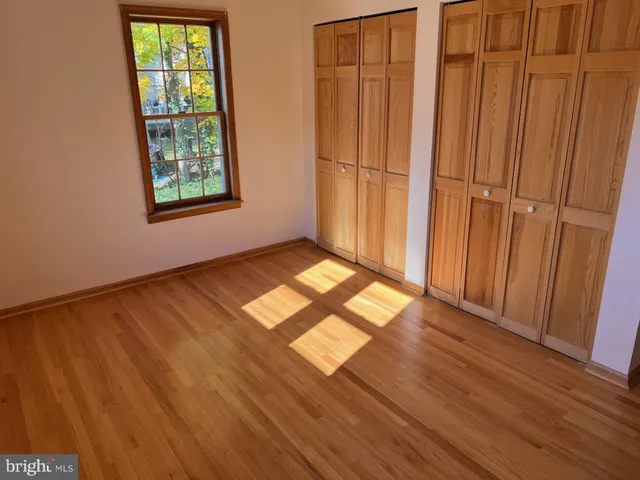 an empty room with wooden floor closet and windows