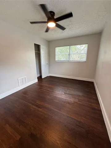 an empty room with wooden floor chandelier fan and windows
