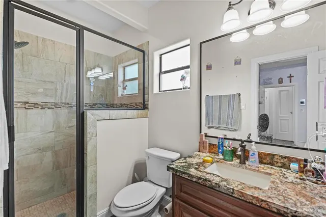 a bathroom with a granite countertop sink a toilet a mirror and shower