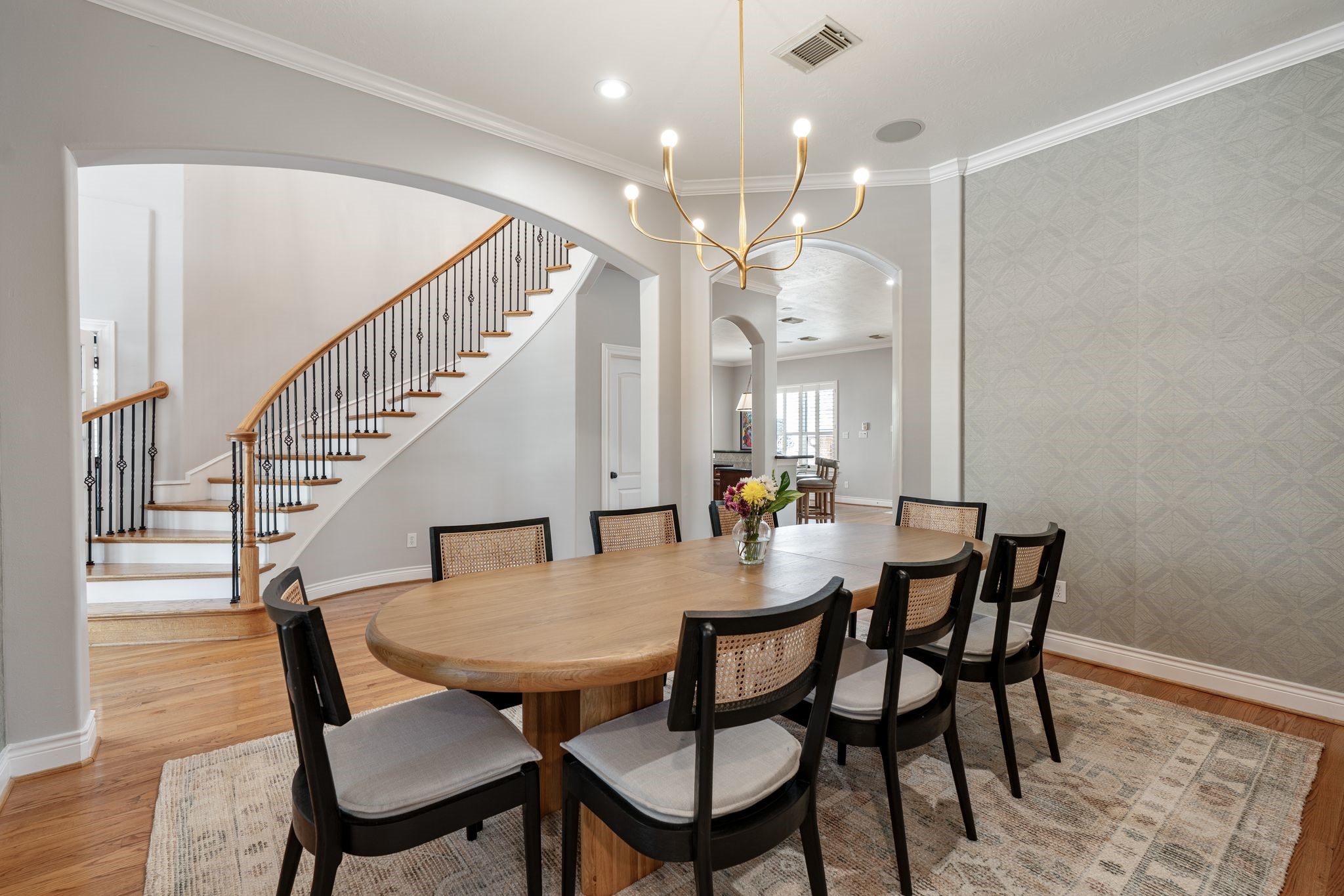 3822 Merrick Street Houston, TX 77025 - Photo 4 of 34 From this vantage point, the sweeping curved staircase becomes a stunning focal point just beyond the dining room. The staircase features a stained wood handrail, ornamental iron balusters, and white painted risers — all visible through a wide arched opening. The open sightline through to the kitchen and beyond speaks to the home's excellent flow.
