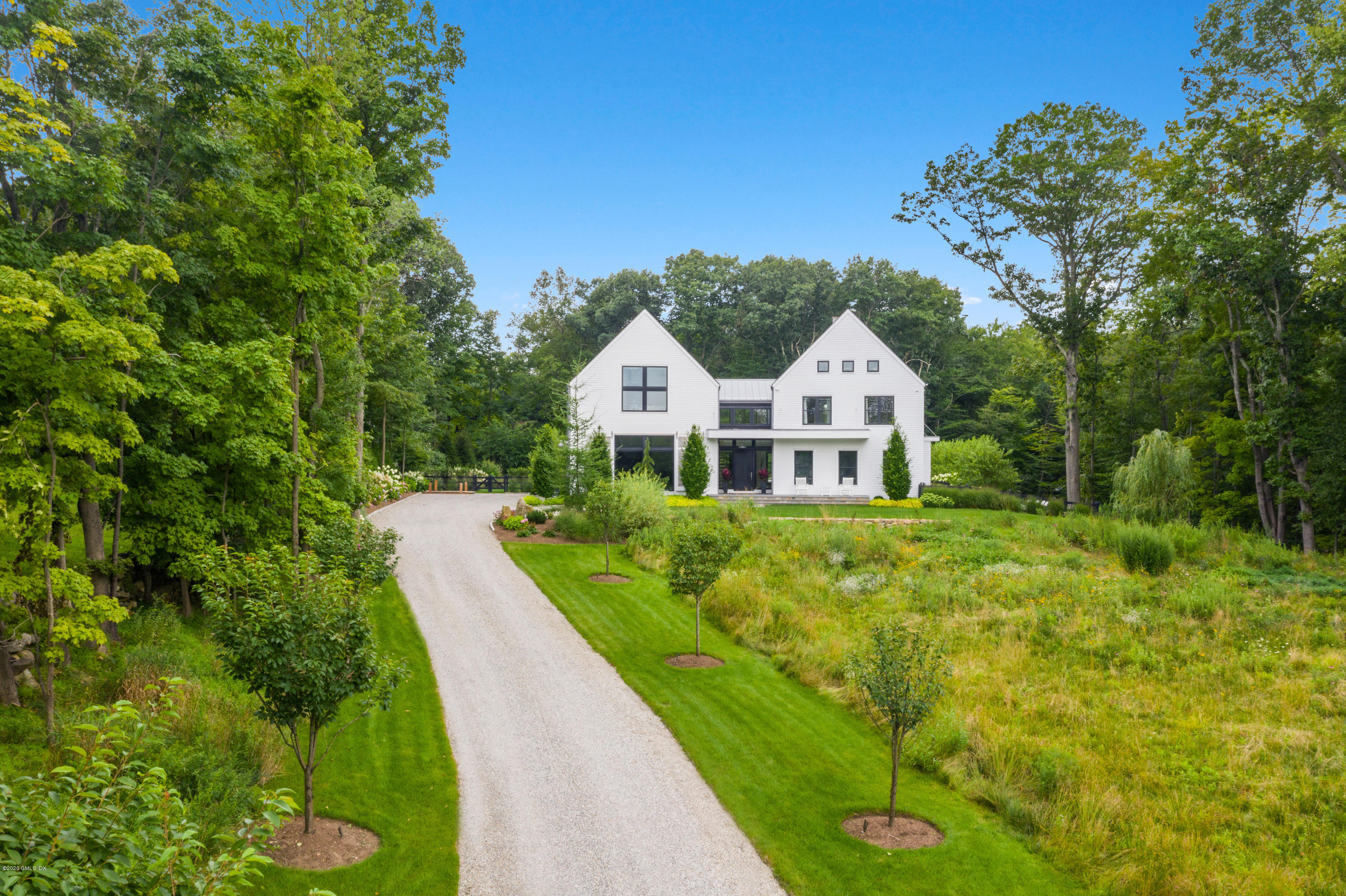 a white house with a big yard plants and large trees