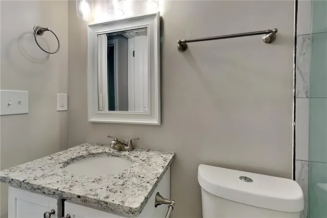 a bathroom with a granite countertop sink a toilet and a mirror
