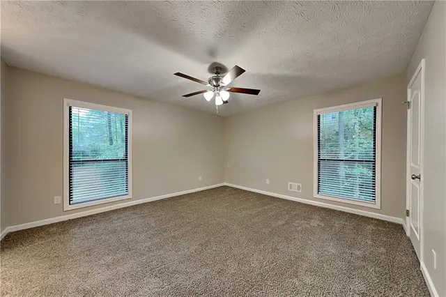 an empty room with chandelier fan and windows