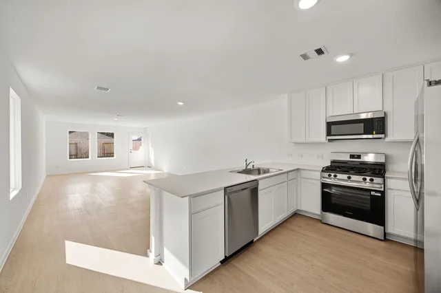 a kitchen with stainless steel appliances granite countertop a stove top oven a sink a refrigerator and white cabinets with wooden floor