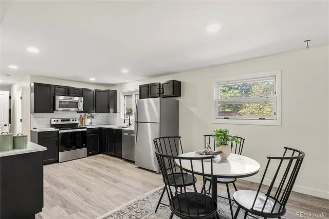 a kitchen with stainless steel appliances kitchen island granite countertop a refrigerator a stove a sink a dining table and chairs with wooden floor