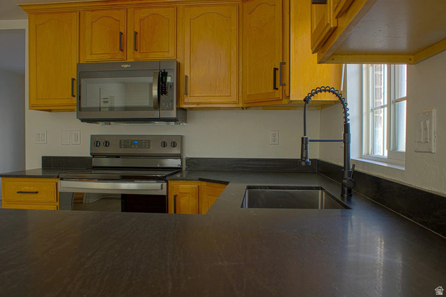 1115 North Main Street Bountiful, UT 84010 - Photo 15 of 17 Kitchen featuring dark countertops, a stainless steel sink with a black high-arc faucet, honey-toned cabinetry, and a window providing natural light