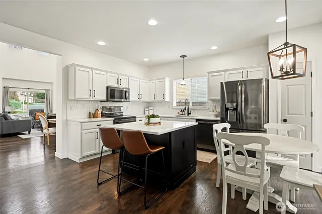 a kitchen with stainless steel appliances granite countertop a sink dishwasher a refrigerator and a dining table with wooden floor