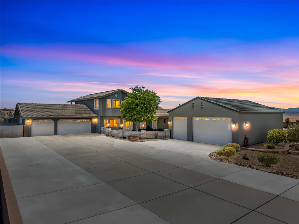 The property features a spacious paved driveway, a main residence with an attached three-car garage, and a detached three-car garage, all under a vibrant sky
