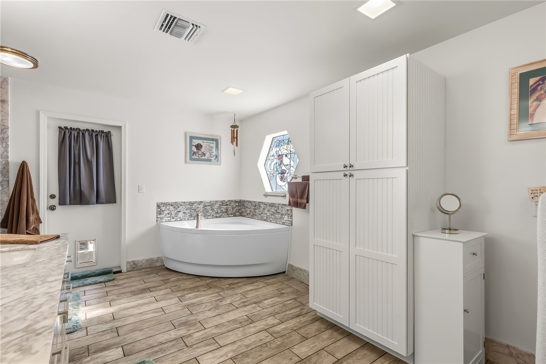 3342 Park Ridge Avenue Bullhead City, AZ 86429 - Photo 51 of 93 Bathroom featuring a corner soaking tub, wood-look tile flooring, and white storage cabinetry